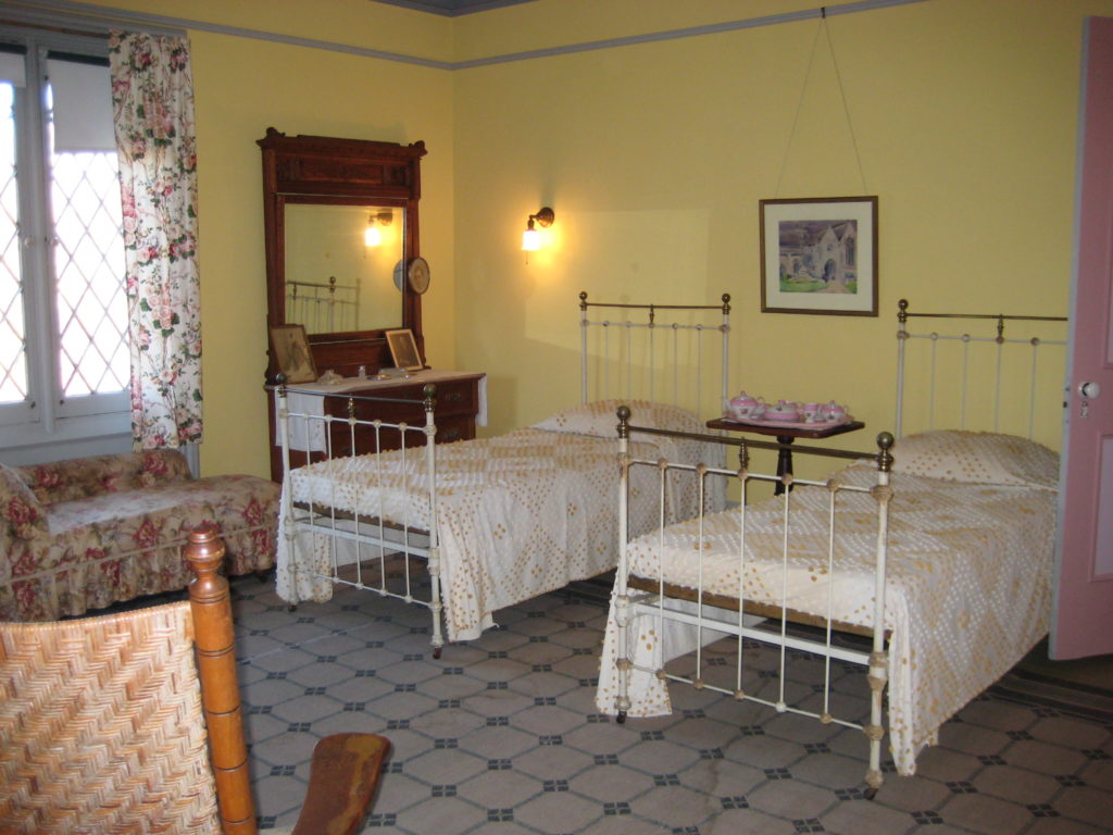 Yellow room with twin beds, bureau with mirror, rug, pink breakfast set on table between beds