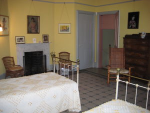 Yellow room with twin beds, fireplace, and two doors, one closed, one open to green servant's hall area.