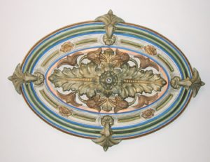 Oval multi-colored medallion in high relief with ornate leaves in center.