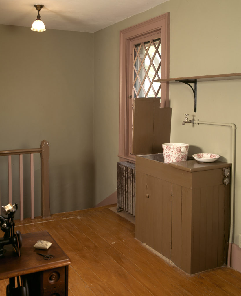 Pale green room with sewing machine and dry sink, at top of stairs with simple bannister