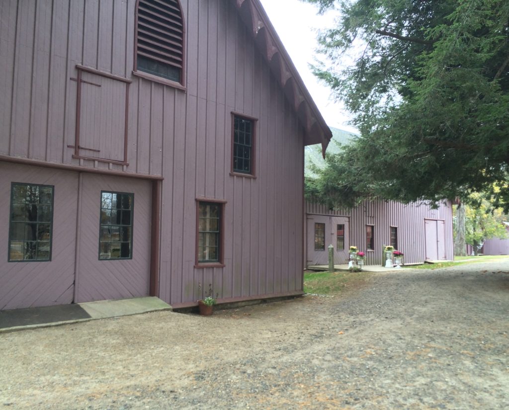 Exterior of purple barn with gravel drive in front. Barn has several bays and Gothic revival elements.