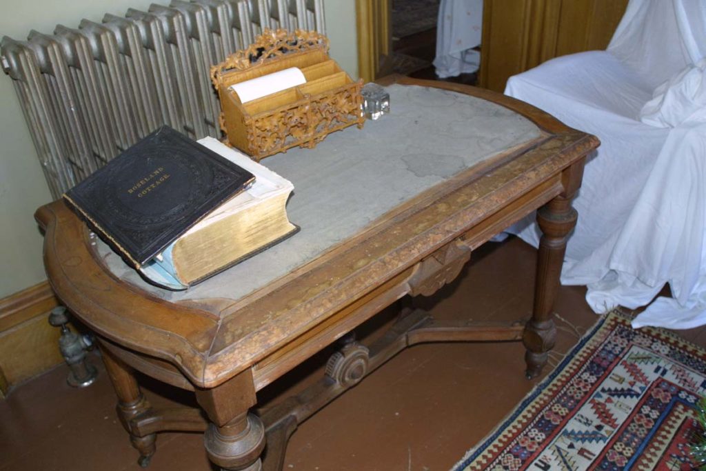 Worn water-spotted wooden desk with faded water-stained felt insert, large book with detached spine on desk.