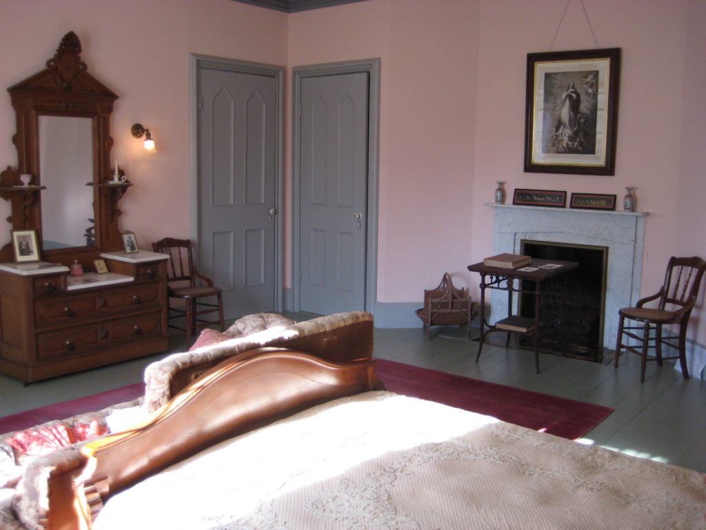 pink room with bureau with mirror, two doors in corner with pointed arch panels
